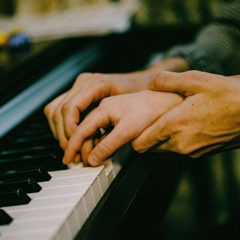 hand helping smaller hand to play piano